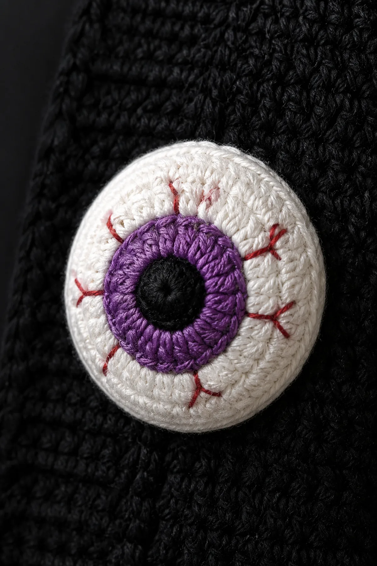 bone-white crochet eyeball applique with a raised jewel-toned iris and fine red embroidered veins
